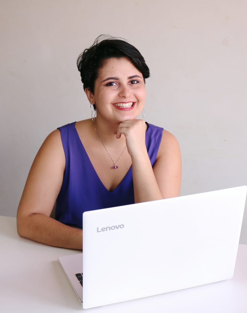 Kássia Magalhães sorrindo, com a mão apoiada no queixo, diante de um notebook branco
