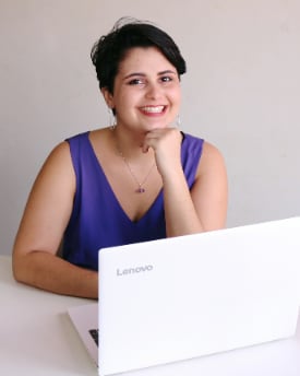 Kássia sorrindo com a mão apoiada no queixo, diante de um notebook branco